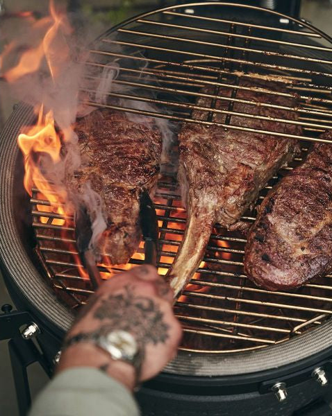 Close up image of steak and chicken on a grill top with fire blazing around the food